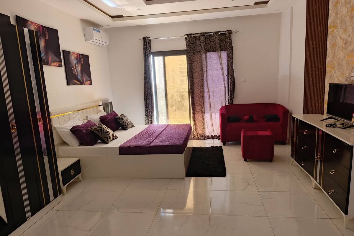 A modern bedroom with a bed, a red sofa, a TV, and a wardrobe.