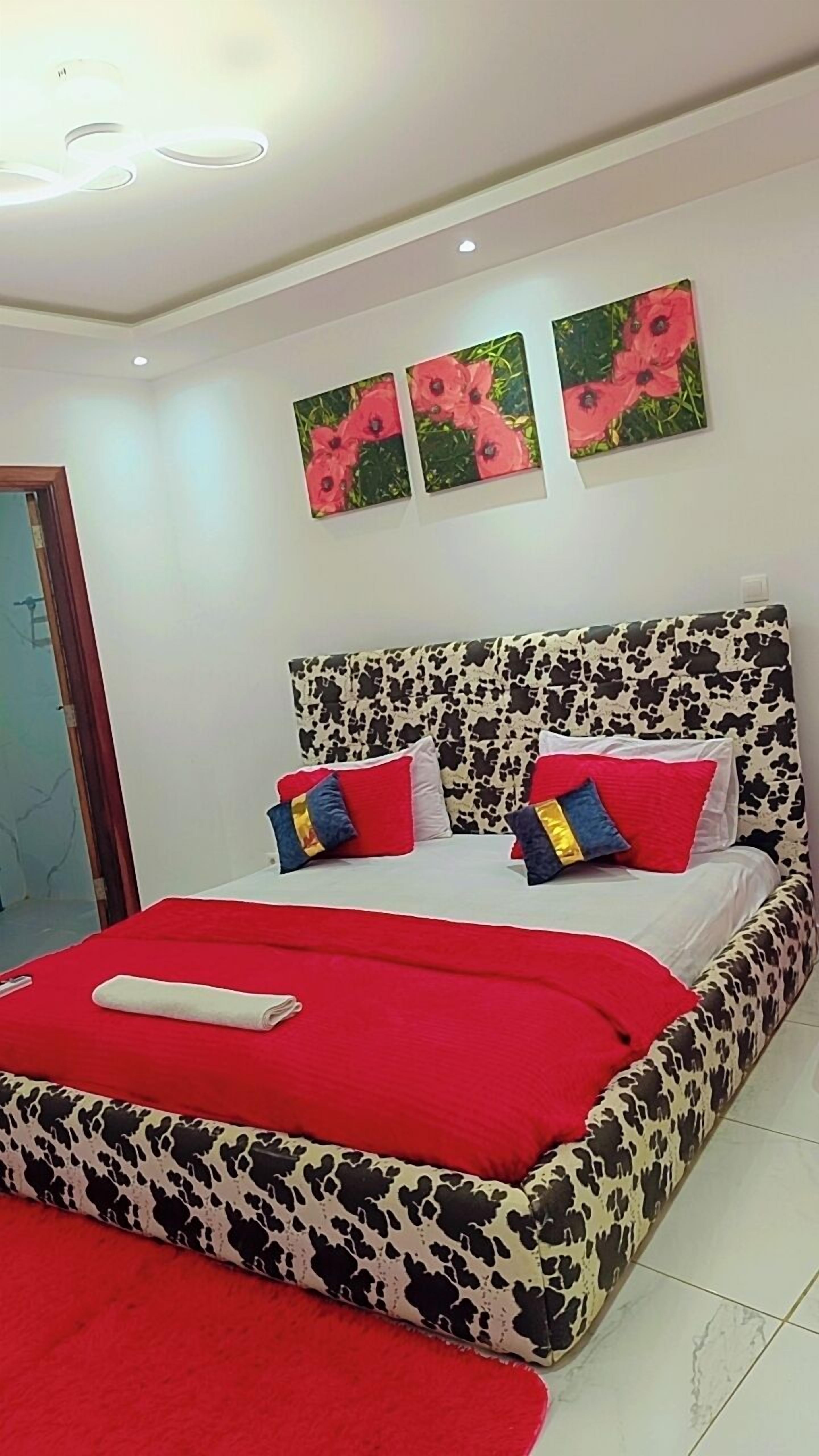 A modern bedroom with a cow print bedspread, a red blanket, and two wall-mounted flower paintings.