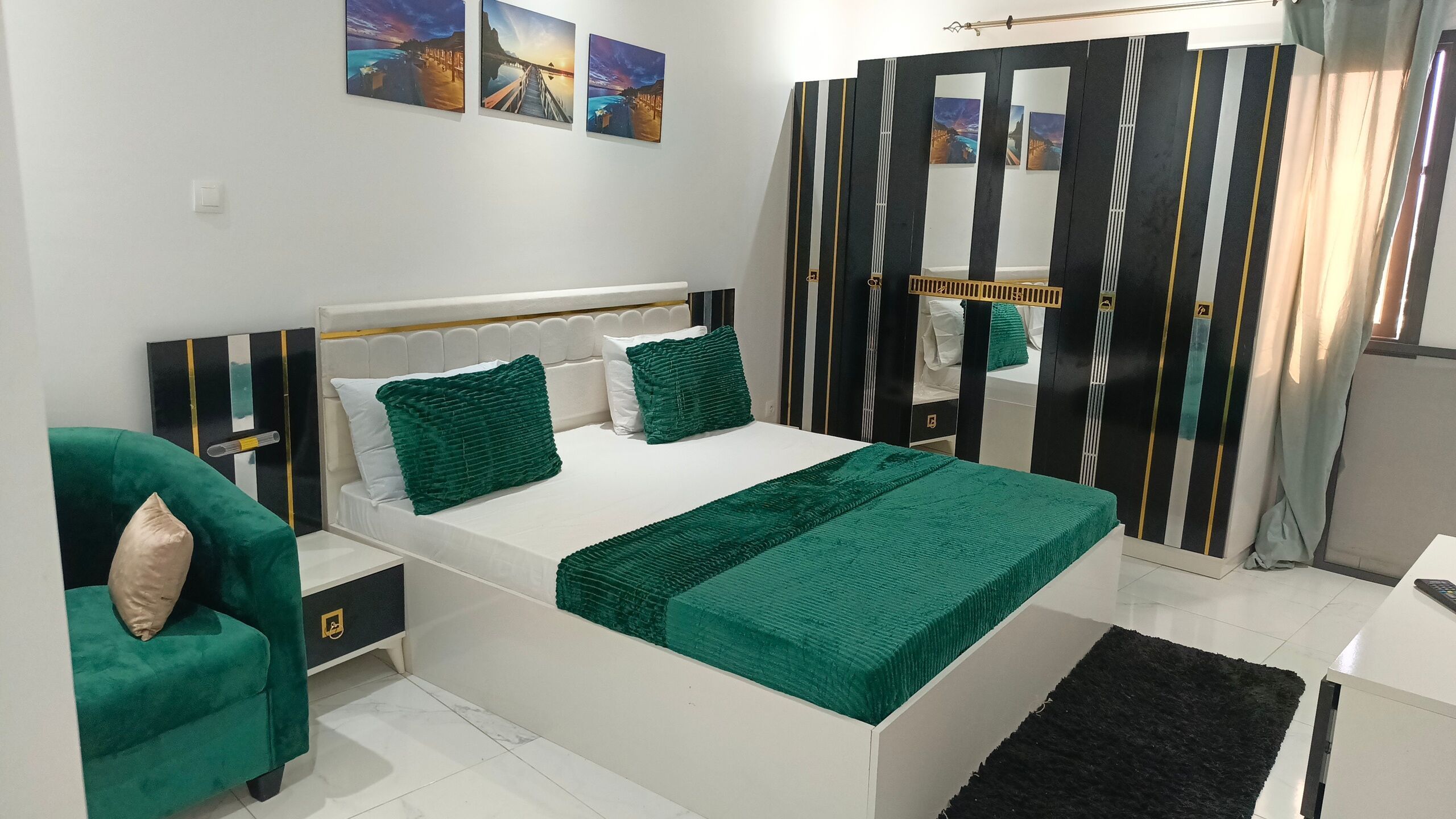 A modern bedroom with a bed, green pillows, a nightstand, a green armchair, a mirror, and artwork on the wall.