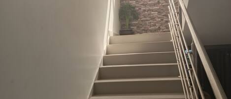A staircase with a metal railing, leading to a room with a stone wall and a window.