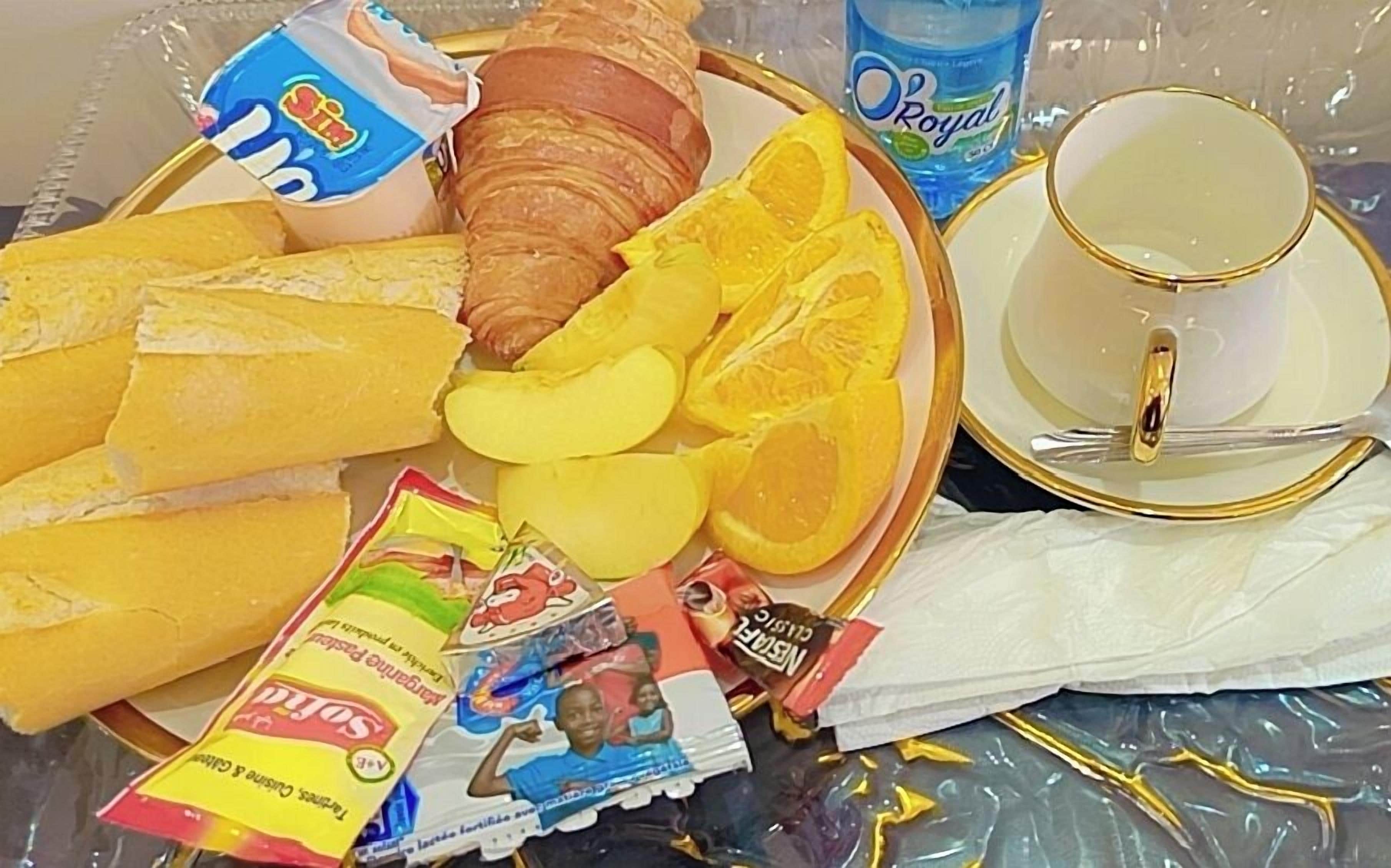 A breakfast tray with croissants, orange slices, a bottle of water, a cup, and a packet of snacks.