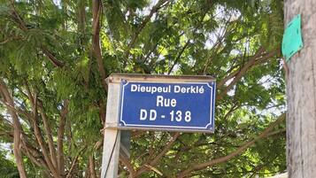 Un cartello stradale con la scritta "Dieupéul Derklé Rue DD-138" sullo sfondo di una fitta vegetazione verde.
