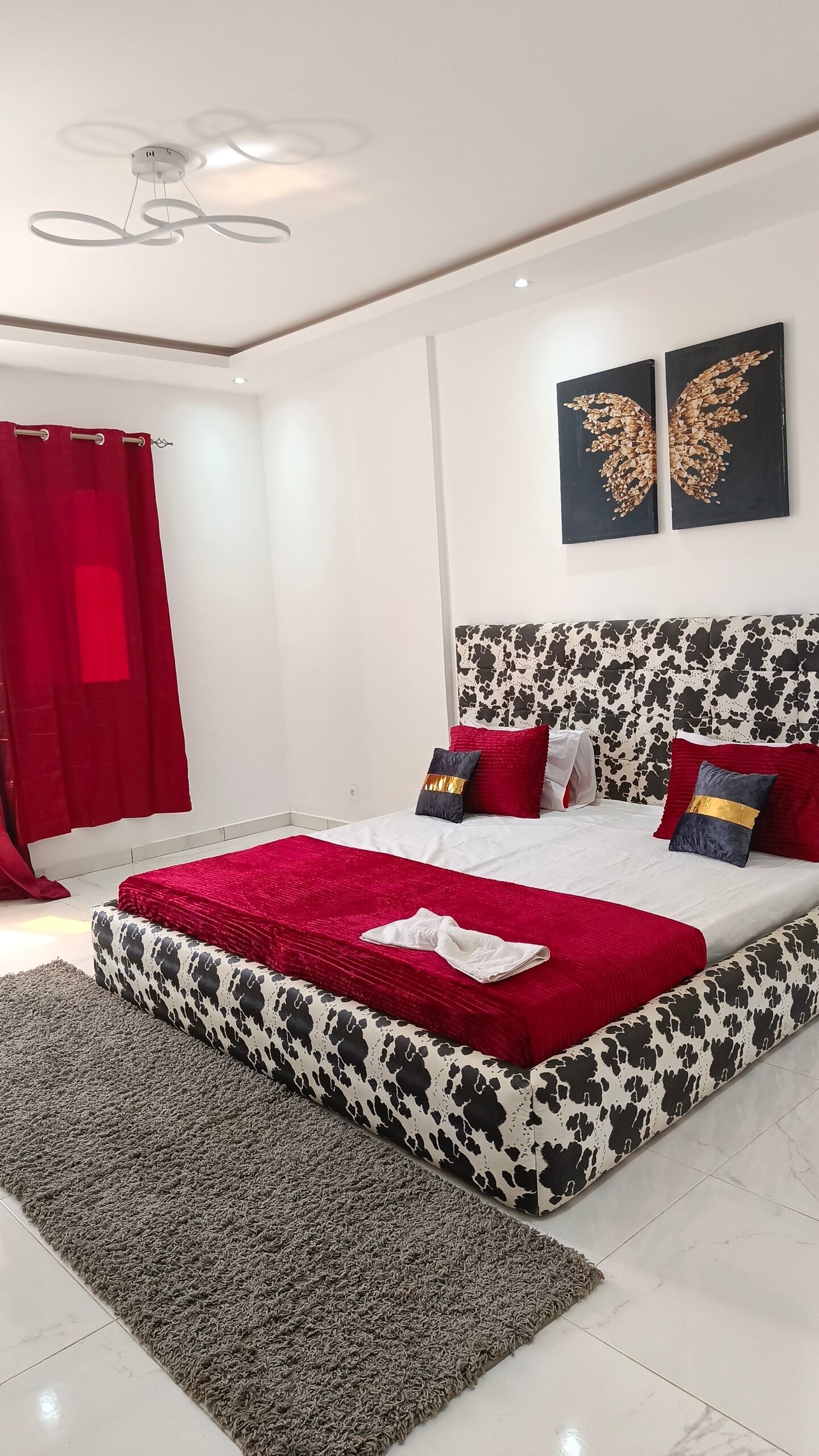 A modern bedroom with a large bed, a red and black patterned headboard, and two wall-mounted butterfly art pieces.
