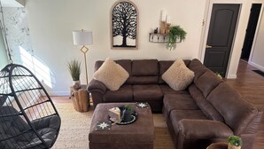 A modern living room with a sectional sofa, a hanging chair, and a coffee table. - One of a kind 4-bedroom barndominium in Warsaw, Ohio on 23 wooded acres. (Warsaw)