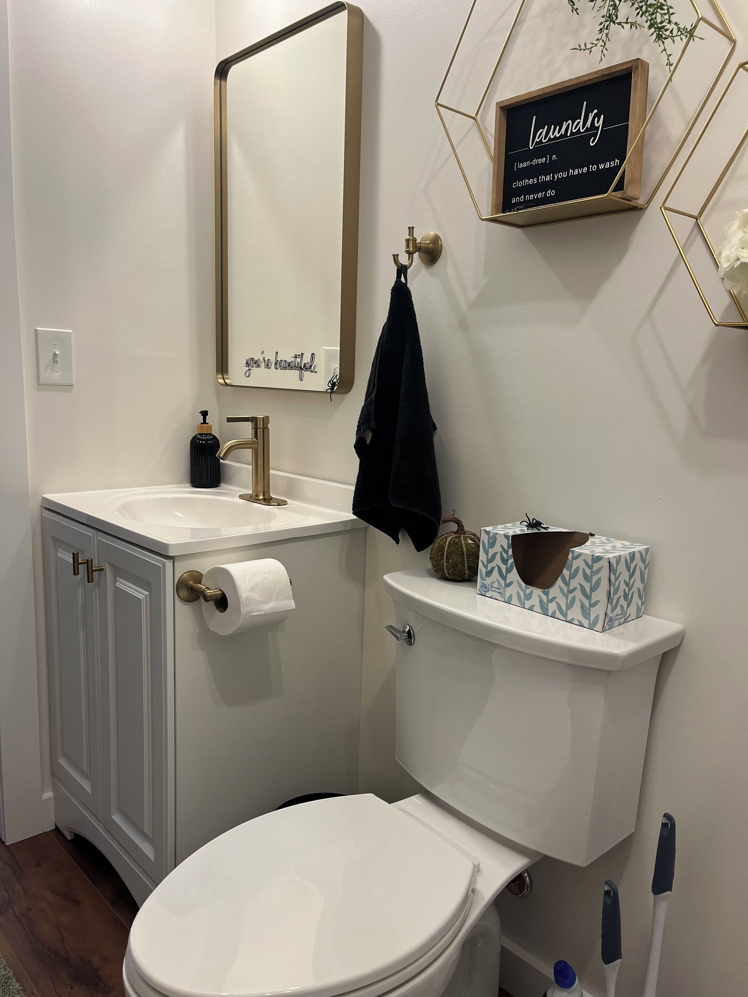 Une salle de bain avec des toilettes, un lavabo et un miroir. Une serviette est accrochée au mur et il y a une pancarte avec le mot « linge ».