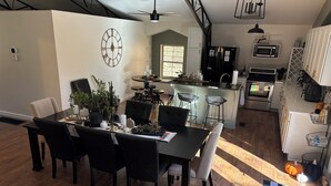 A modern kitchen with a central island, a dining area with a black table and chairs, and a ceiling fan. - One of a kind 4-bedroom barndominium in Warsaw, Ohio on 23 wooded acres. (Warsaw)
