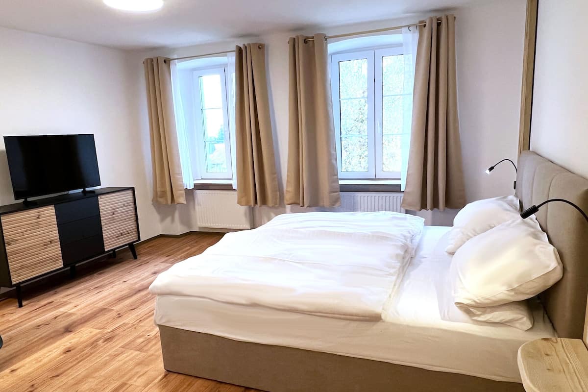 Quarto com cama, TV em um móvel e janelas com cortinas.