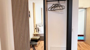 Een moderne kamer met een houten vloer, een garderobe met spiegel en een klein zithoekje met een stoel en tafel.