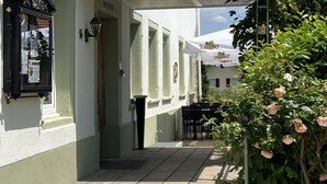 Een gebouw met een pannendak, een overdekte ingang en een pad van stenen tegels dat leidt naar een terras.