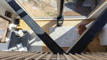 Una habitación con tragaluz, cama con somier de madera, una pequeña zona de estar y ventana con vistas al exterior.