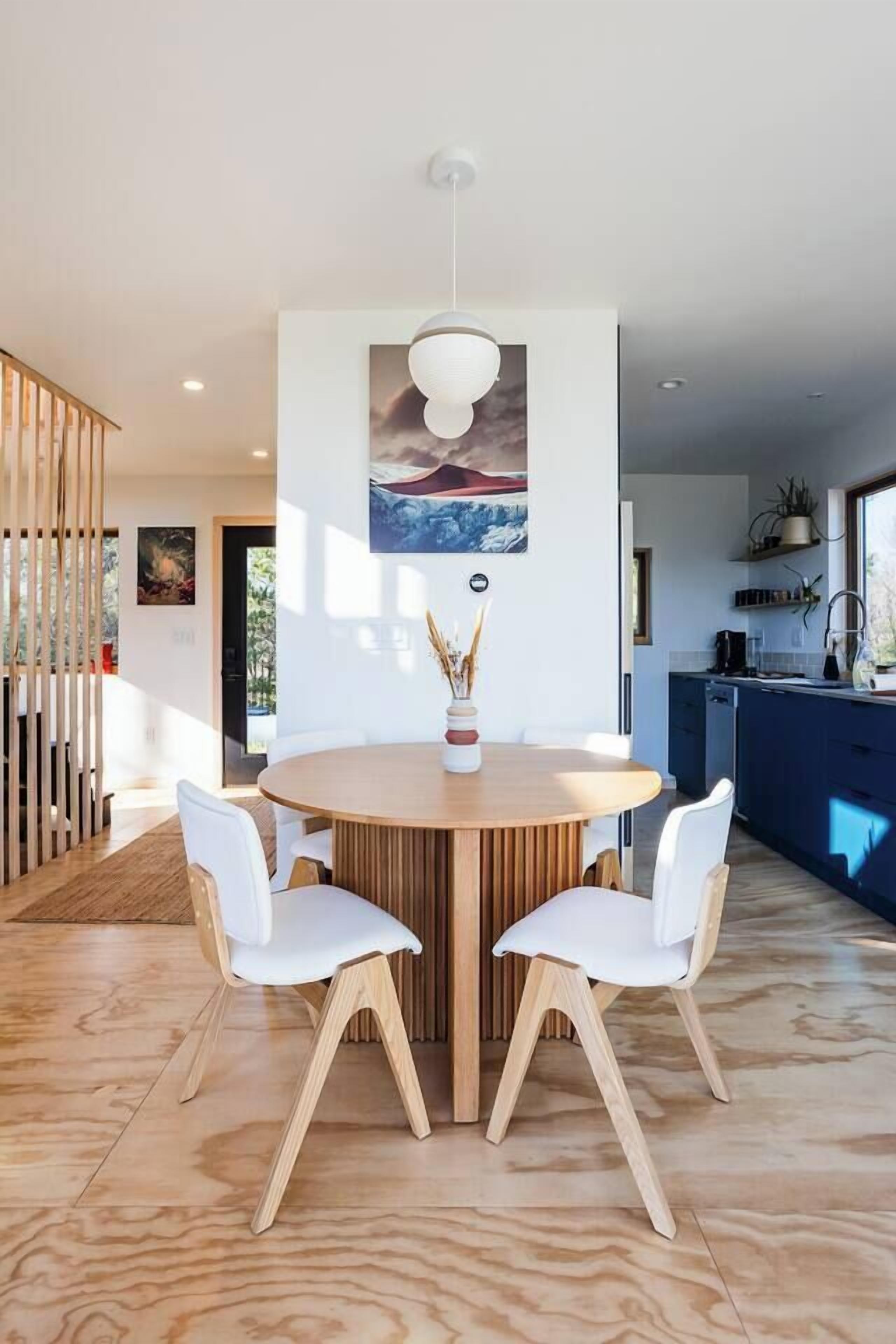 A modern dining area with a round wooden table, white chairs, and a pendant light.
