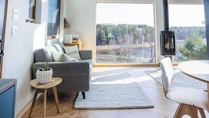A modern living room with a sofa, a small table, and a chair. There is a large window providing a view of the outdoors. - Lakeside Loft, Roof Deck + Sauna (Phelps)