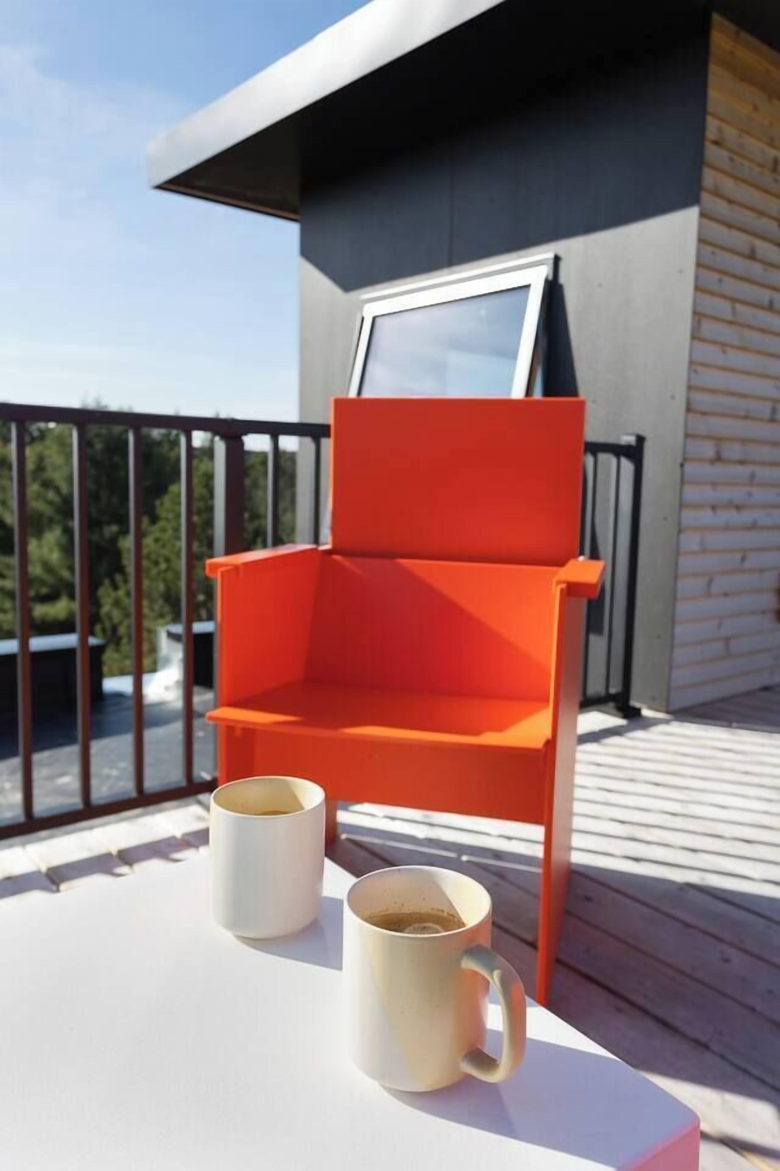 A balcony with a red chair and two white mugs on a white table.