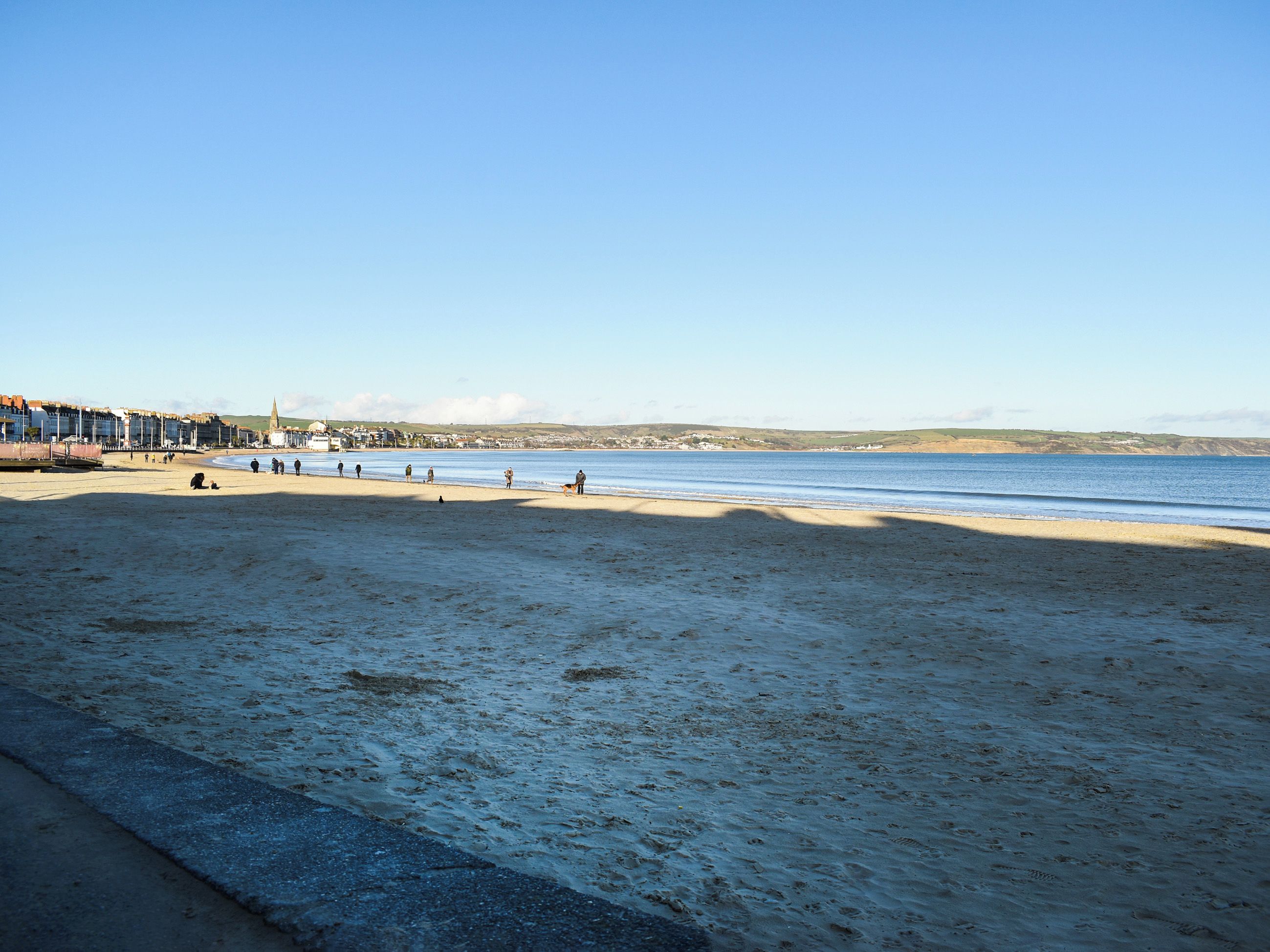 A beach with a clear sky, sandy shore, and a few people.