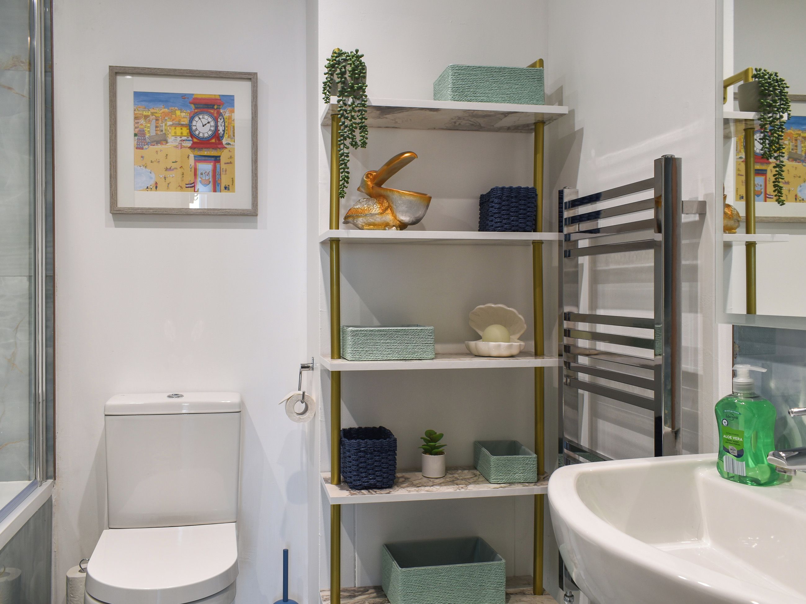A bathroom with a toilet, a sink, a mirror, and shelves with decorative items.