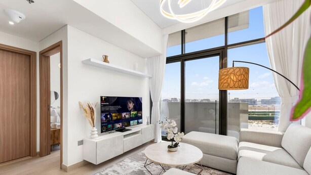 A modern living room with a large flat-screen TV, a round coffee table, and a sofa. - Urban Chic 1BR in Dubai (Dubai)