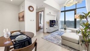 A modern living room with a dining area, a television, and a large window with a city view. - Urban Chic 1BR in Dubai (Dubai)