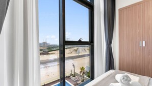 A hotel room with a large window offering a view of a beach and a swimming pool. - Urban Chic 1BR in Dubai (Dubai)