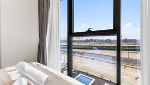 A hotel room with a large window, a bed with a rolled white towel, and a view of a beach and buildings. - Urban Chic 1BR in Dubai (Dubai)