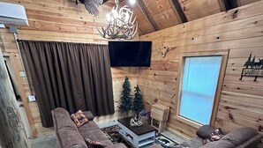 A log cabin interior with a brown couch, a small table, a TV, and a chandelier.