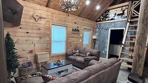 A cozy wooden interior with a sofa, a chandelier, and a ladder.