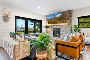 Una sala de estar moderna con chimenea de piedra, ventanas amplias y vistas al exterior.