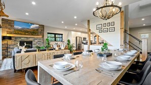 Un comedor amplio con una mesa de madera larga dispuesta para una comida, una chimenea y una cocina moderna al fondo.