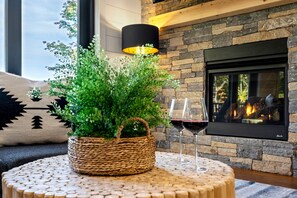 Una sala de estar acogedora con chimenea de piedra, un centro de mesa con planta tejida y dos copas de vino.