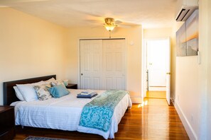 Une chambre à coucher avec un lit, des tables de chevet, un ventilateur de plafond et une porte.