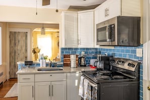 A modern kitchen with white cabinets, a stainless steel microwave, a stove, and a blue tiled backsplash. - Steps from the ocean - minutes from Boston (Winthrop)