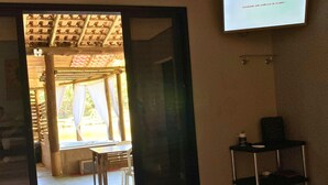A hotel room with a bed, a small table, a chair, a TV mounted on the wall, and a view of an outdoor area with a wooden structure and a pool. - Recanto Elter (Piracaia)