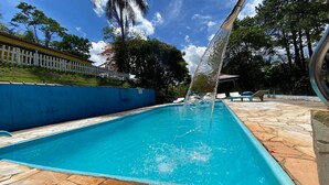 A swimming pool with clear blue water, surrounded by a stone deck and a white fence. - Recanto Elter (Piracaia)