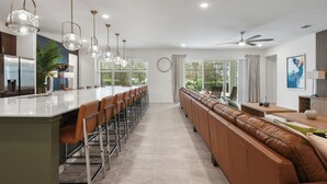 A modern kitchen with a long island, bar stools, and pendant lighting. - Luxury 15-Bedroom home with Pool, Spa, Theater & Near Theme Parks (Kissimmee)