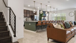 A modern kitchen with dark cabinets, a central island, and pendant lighting. - Luxury 15-Bedroom home with Pool, Spa, Theater & Near Theme Parks (Kissimmee)