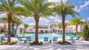 A poolside area with palm trees, lounge chairs, and a building in the background. - Luxury 15-Bedroom home with Pool, Spa, Theater & Near Theme Parks (Kissimmee)