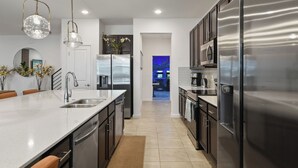 A modern kitchen with stainless steel appliances, a large island, and pendant lighting. - Luxury 15-Bedroom home with Pool, Spa, Theater & Near Theme Parks (Kissimmee)