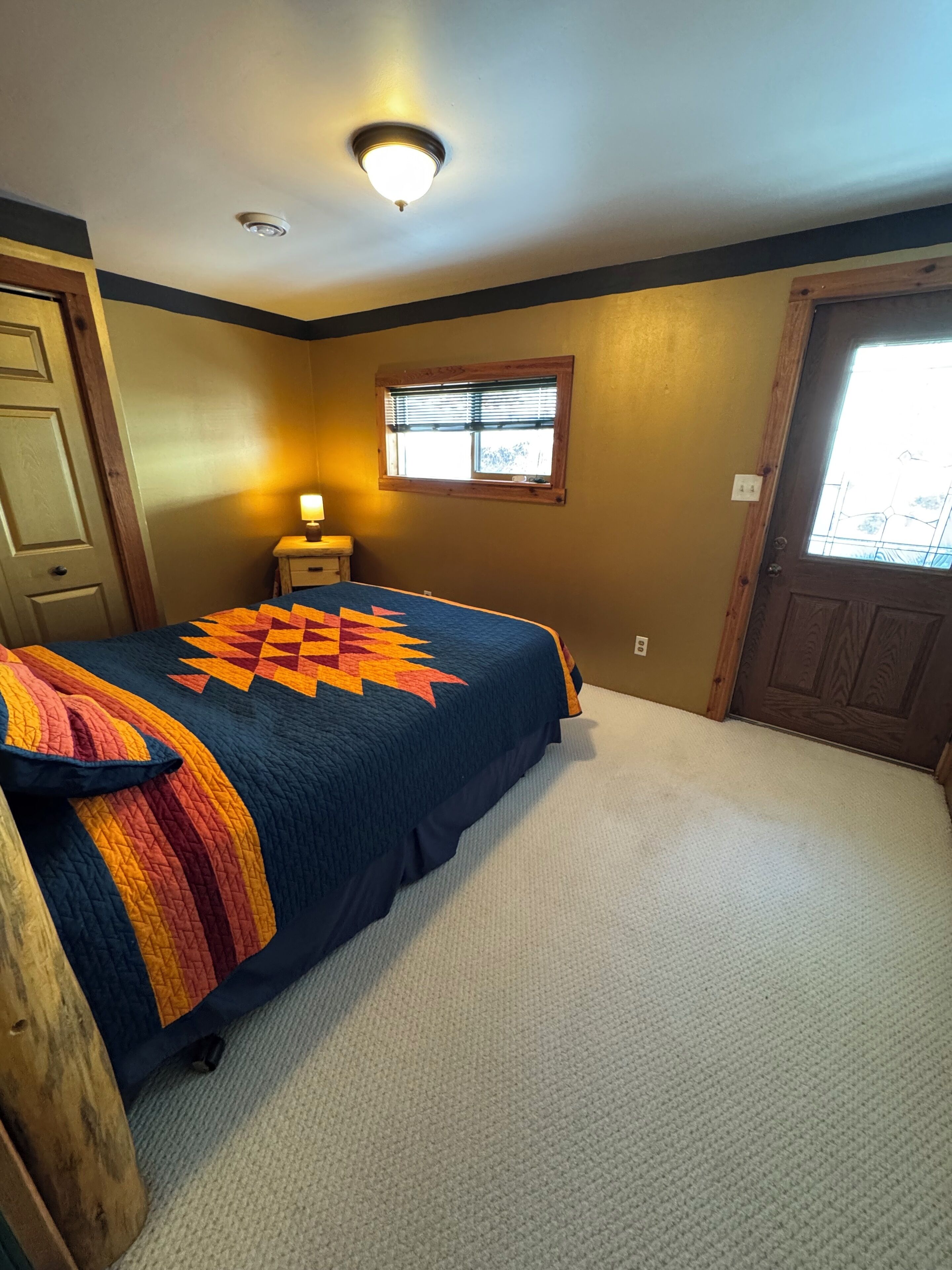 A bedroom with a bed, a nightstand, a window, and a door.