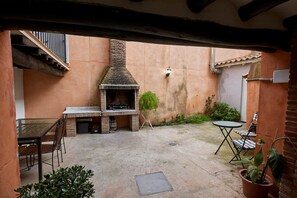 Terrassa exterior amb forn de rajola, taula amb cadires i plantes en testos.