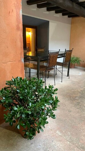 Terrassa exterior amb taula i cadires, una planta en test i una paret amb una porta que dóna a un espai interior.
