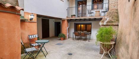 A courtyard with a dining table and chairs, a potted plant, and a small table with a chair.