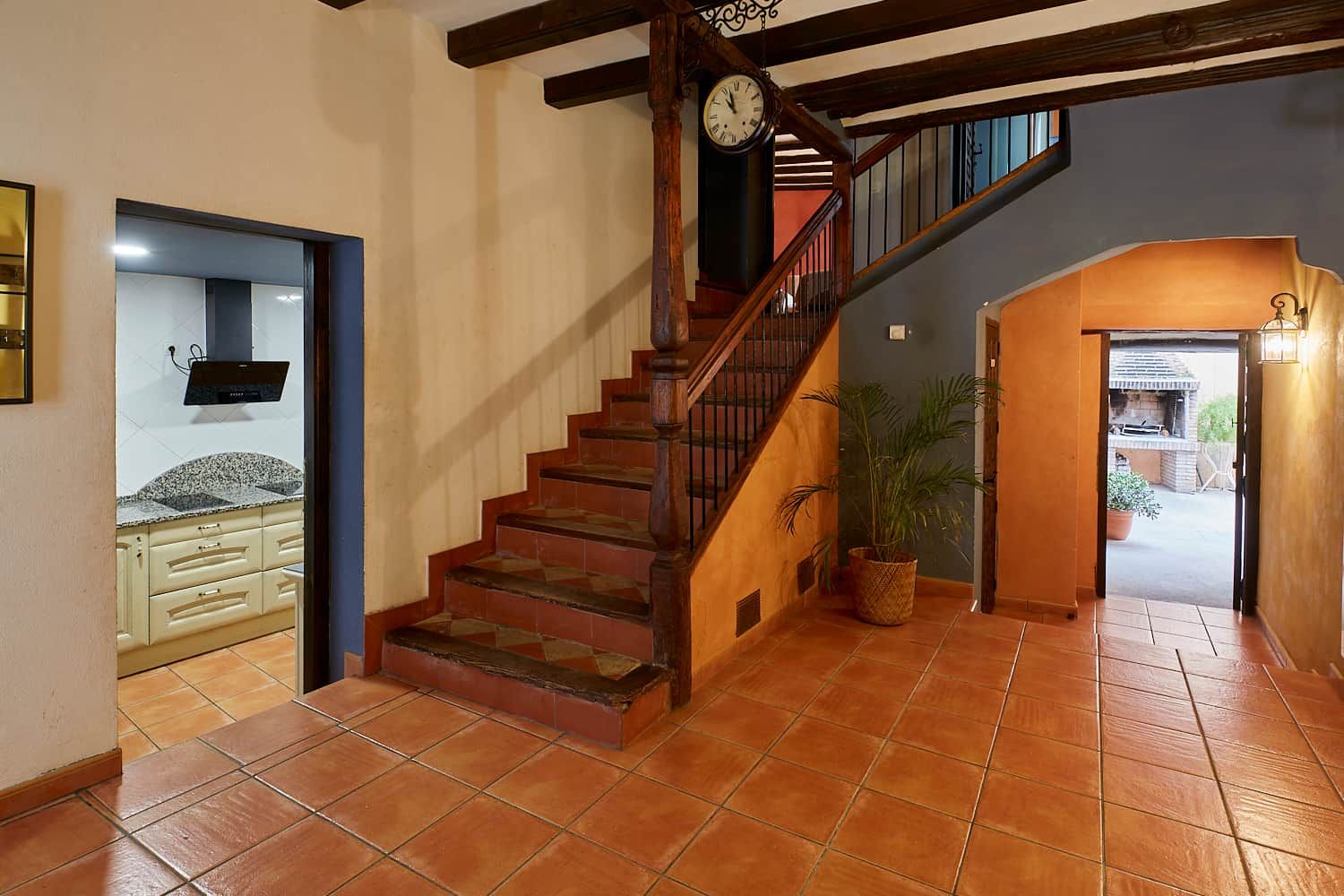 A staircase with wooden steps and a clock, leading to a kitchen area with cabinets and a countertop.