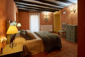 Une chambre à coucher avec un lit, des lampes de chevet, une commode, un radiateur et une fenêtre avec des rideaux.