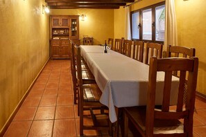 A dining area with a long table, wooden chairs, and a kitchen in the background. - Pajarilla de Cosuenda Country House (Cosuenda)