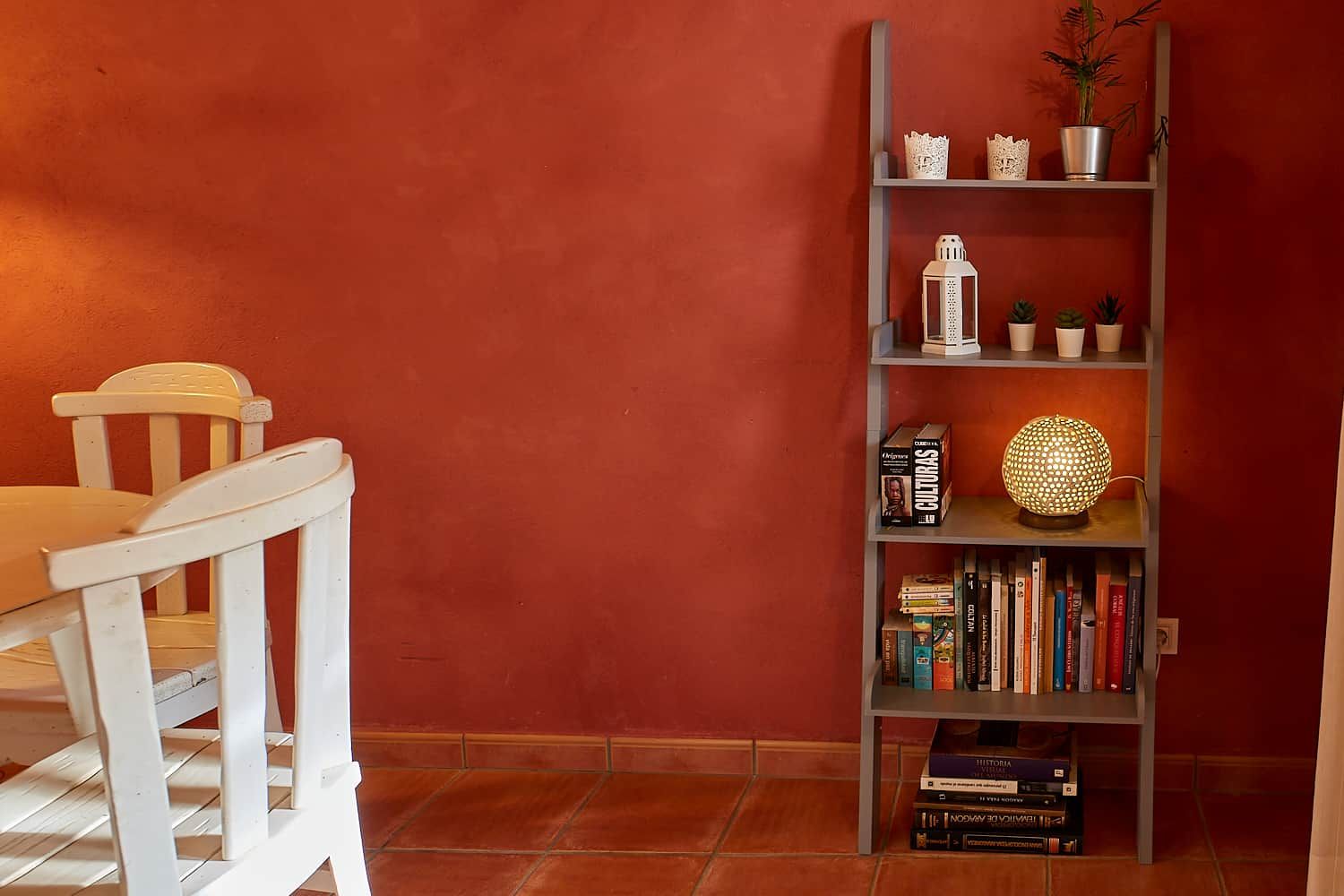 Una habitació amb una cadira blanca, una prestatgeria plena de llibres i objectes decoratius, i una paret vermella.