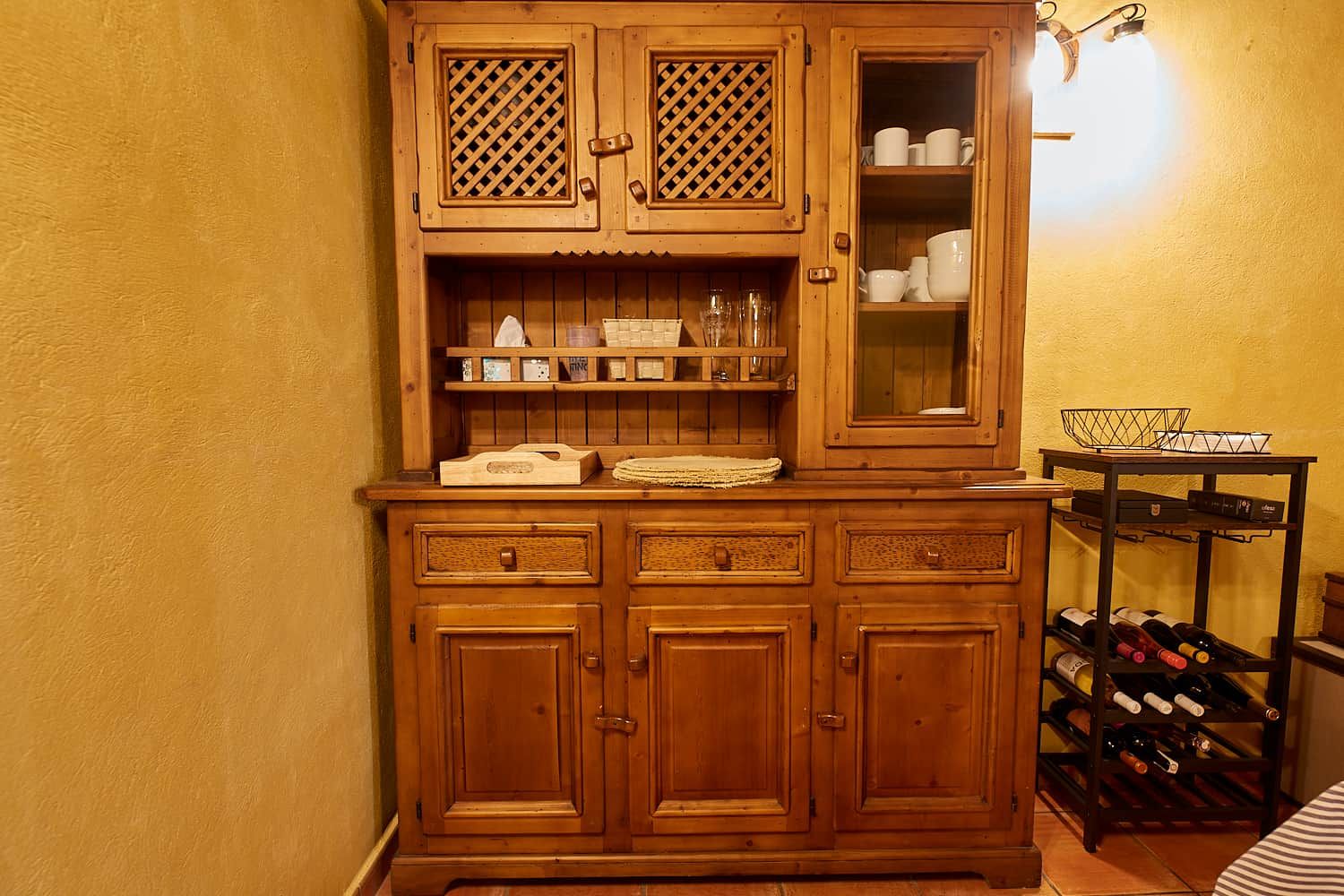 A wooden cabinet with drawers and shelves, a wine rack with bottles, and a light fixture on the wall.