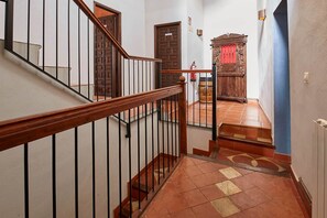 Una escala amb barana de fusta i ralla metàl·lica que condueix a una habitació amb terra de rajola i un armari de fusta.