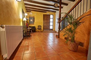 A hallway with a tiled floor, a wooden staircase, a door, and a potted plant.
