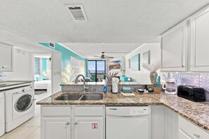 A modern kitchen with a built-in dishwasher, double sink, and a view of the outdoors. - Oceanfront 3BR Condo • Balcony Beach Views • Indoor Pool & Hot Tub (North Myrtle Beach)