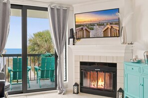 A living room with a fireplace, a TV mounted above it, and a balcony with chairs. - Oceanfront 3BR Condo • Balcony Beach Views • Indoor Pool & Hot Tub (North Myrtle Beach)