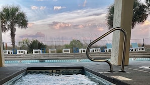 Una piscina con agua cristalina, una escalera metálica y, al fondo, palmeras y una valla.